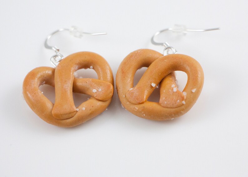 Puede incluir: Un par de pendientes de pretzel con sal y ganchos plateados. Los pretzels est&aacute;n hechos de arcilla polim&eacute;rica y tienen un aspecto realista.