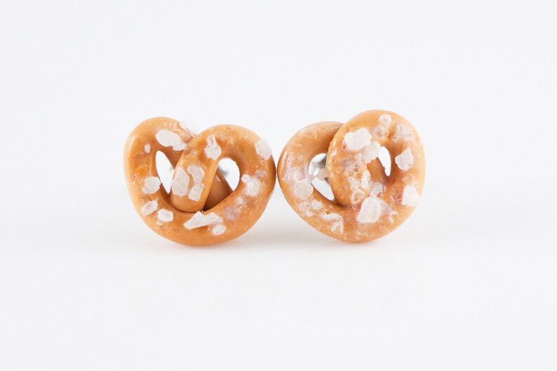 May include: A pair of salt-covered pretzel earrings. The earrings are made of polymer clay and are a light brown color.