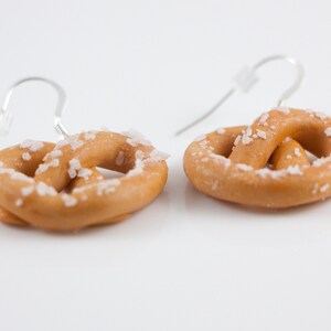 Puede incluir: Un par de pendientes de pretzel de plata con un dise&ntilde;o de pretzel cubierto de sal.