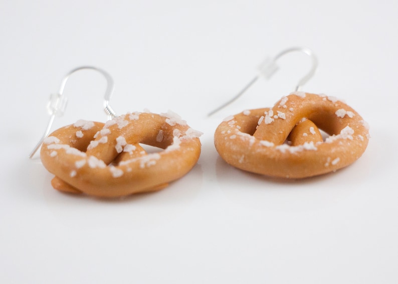 Puede incluir: Un par de pendientes de pretzel de plata con un dise&ntilde;o de pretzel cubierto de sal.