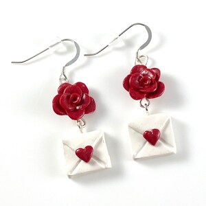 May include: A pair of dangle earrings featuring a red rose and a white envelope with a red heart on each earring.