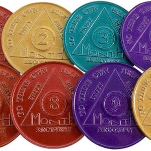 Puede incluir: Doce fichas metálicas redondas de color plateado, dorado, rojo, morado y verde azulado con un diseño triangular. Cada ficha tiene un número del 1 al 12 y las palabras "To thine own self be true" y "Month of Recovery".