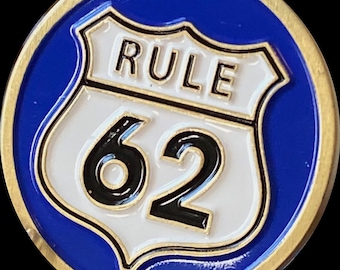 以下が含まれることがあります： 青い背景に金色の丸いピン。ピンには、黒い数字「62」と黒い文字で「RULE」と書かれた白い盾が描かれています。