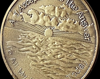 May include: A gold-toned metal token with the words "And Acceptance Is The Answer To All My Problems Today" engraved around the edge. The centre of the token features a raised image of a sun rising over a wavy sea with clouds in the sky.