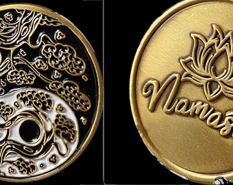 May include: A gold-colored coin with two sides. One side features a black and white yin yang symbol with a tree design. The other side features a gold lotus flower and the word "Namaste" in a stylized font.