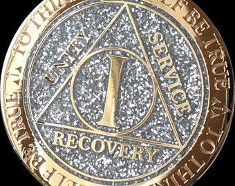 May include: Gold-colored coin with a silver glitter finish. The coin features a triangle with the words "Unity", "Service", and "Recovery" inscribed on each side. The center of the coin has the number "1" and the words "To Thine Own Self Be True" are inscribed around the outer edge.