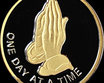 Puede incluir: Manos doradas en oración sobre un fondo negro con el texto "ONE DAY AT A TIME".