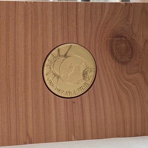 May include: A wooden box with a gold-colored metal medallion inset. The medallion features a stylized sun, earth, and moon with the text "One Day At A Time".