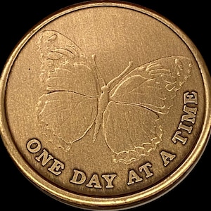 May include: A gold-colored metal token with a butterfly design and the text "One Day At A Time".