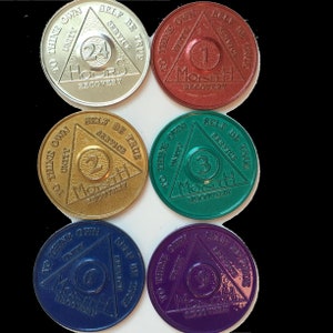 May include: Six round, metallic tokens with a triangle design. Each token features a different color and number, representing a time period of recovery: 24 hours, 1 month, 2 months, 3 months, 6 months, and 9 months. The text on each token reads "To thine own self be true, Unity, Service".