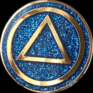 May include: A gold-colored coin with a blue glitter background and a gold triangle in the center. The triangle is outlined in gold and has a gold border.