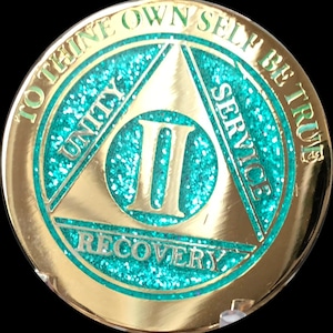 May include: Gold-colored coin with a teal green triangle design. The triangle has the words "Unity", "Service", and "Recovery" inscribed on each side. The number "II" is in the center of the triangle. The words "To thine own self be true" are inscribed around the outside of the coin.