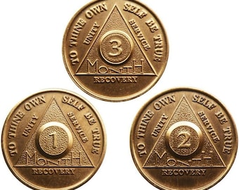 May include: Three gold-colored metal coins with a triangle design. Each coin has the words "To Thine Own" and "Self Be True" on the top and bottom of the triangle. The words "Unity" and "Service" are on the left and right sides of the triangle. The center of each coin has the number "1", "2", or "3" and the word "Month" below it. The words "Recovery" are at the bottom of each coin.
