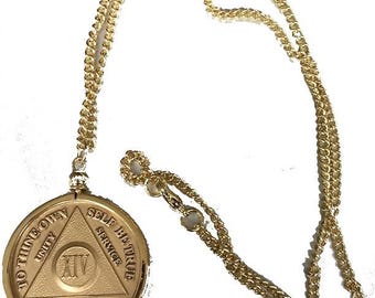 May include: A gold-coloured metal necklace featuring a circular pendant with a central triangle. The pendant is embossed with the Roman numeral XIV, the words Unity, Service, Recovery, and the phrase To Thine Own Self Be True along the outer edge.