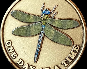 May include: A gold-colored coin with a dragonfly design and the text "One Day At A Time" around the edge.