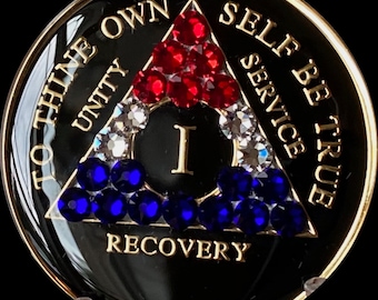 May include: A black and gold coin with a red, white, and blue triangle design. The triangle has the words "To Thine Own Self Be True" and "Unity, Service, Recovery" around it. The center of the triangle has the number "I" in gold.