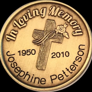 May include: A gold-toned memorial coin with the inscription "In Loving Memory" around the edge. A wooden cross with a rose is in the center. The text "Josephine Petterson 1950 - 2010" is inscribed below the cross.