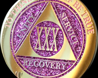 May include: Gold-coloured coin with a purple glitter finish. The coin features a triangle with the words "Unity", "Service", and "Recovery" inscribed around it. The centre of the triangle has the Roman numeral "XXX" and the words "To Thine Own Self Be True" around the outer edge.