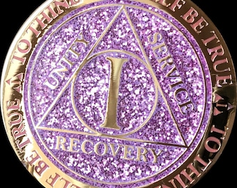 May include: A gold-coloured coin with a purple glitter background. The coin features a triangle with the words "Unity", "Service", and "Recovery" inscribed on each side. The number "1" is in the centre of the triangle. The words "To thine own self be true" are inscribed around the edge of the coin.