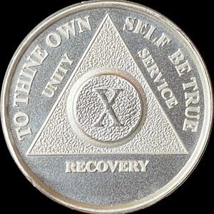 Könnte beinhalten: Eine kreisförmige, silberfarbene Medaille mit einem zentralen Dreieck mit strukturierter Oberfläche. Die römische Ziffer X ist in der Mitte eingeprägt. Der Text TO THINE OWN SELF BE TRUE steht am Rand, zusammen mit UNITY, SERVICE und RECOVERY.