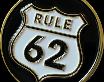 May include: A gold-coloured round coin with a black background. A white shield with a gold outline features the text "RULE" and the number "62" in black.