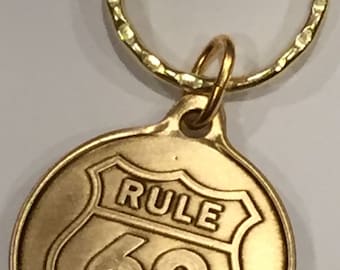 May include: Gold-colored keychain with a round tag featuring a shield-shaped design with the text "RULE 62" inside.
