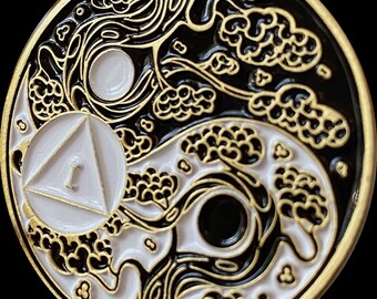 May include: A gold-colored metal coin with a yin yang design. The yin yang is surrounded by a black and white tree design. The coin has a white triangle with the number "1" in the center.