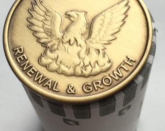May include: A gold-coloured metal token with a phoenix rising from flames and the text "Out of the Ashes of Addiction Renewal & Growth".