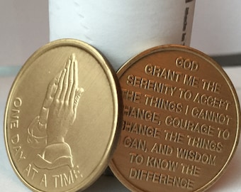 May include: Two gold-coloured metal tokens. One token features a praying hands design with the text "One Day At A Time". The other token features the text "God Grant Me The Serenity To Accept The Things I Cannot Change, Courage To Change The Things I Can, And Wisdom To Know The Difference."