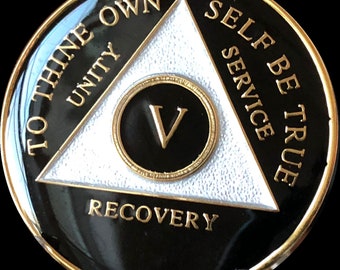 May include: Black and gold coin with a white triangle in the center. The triangle has the words "To Thine Own Self Be True" written around it. The words "Unity", "Service", and "Recovery" are written on the triangle. The number "V" is in the center of the triangle.
