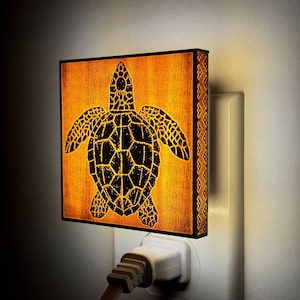 Puede incluir: Una luz nocturna de madera con forma de tortuga marina con una silueta negra. La luz nocturna está enchufada a una toma de corriente.