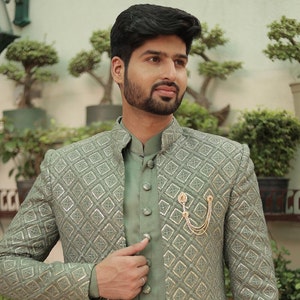 May include: A sage green patterned jacket with a matching sage green shirt underneath. The jacket has a mandarin collar and a gold chain brooch.