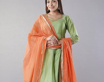May include: A green and orange salwar kameez with gold trim. The kameez is a long, flowing top with a round neckline. The salwar is a pair of loose-fitting trousers. The outfit is completed with a matching orange dupatta.