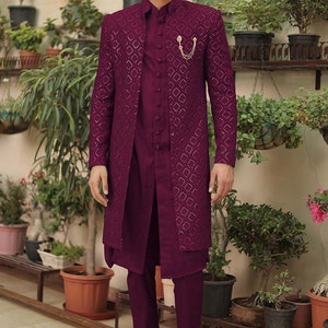 May include: A maroon patterned long-sleeved jacket with a matching maroon shirt and pants. The jacket has a gold chain detail on the front. The man is wearing brown leather shoes.