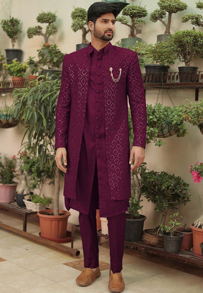 May include: A maroon patterned long-sleeved jacket with a matching maroon shirt and pants. The jacket has a gold chain detail on the front. The man is wearing brown leather shoes.