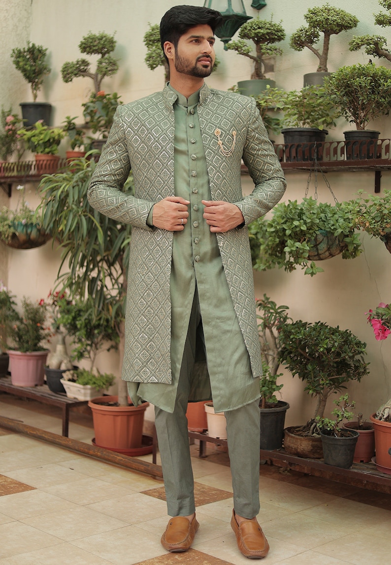 May include: A sage green long-sleeved jacket with a geometric pattern, worn over a matching sage green shirt and pants. The jacket has a mandarin collar and a button closure. The man is wearing brown leather loafers.