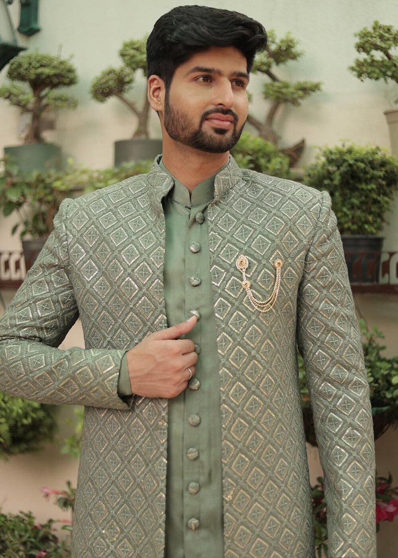 May include: A sage green patterned jacket with a matching sage green shirt underneath. The jacket has a mandarin collar and a gold chain brooch.