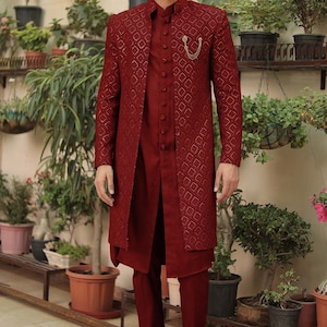 May include: A maroon long-sleeved kurta with a geometric pattern and a matching pair of pants. The kurta has a mandarin collar and a button closure. The man is wearing brown leather loafers.