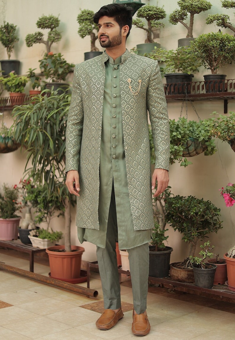 May include: A man wearing a sage green patterned long jacket over a matching sage green kurta and pants. He is wearing brown leather loafers.