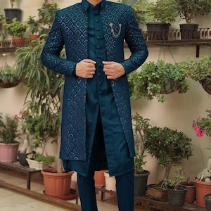 May include: A teal blue three-piece suit with a patterned jacket, a long teal blue shirt, and matching teal blue pants. The man is wearing brown loafers.