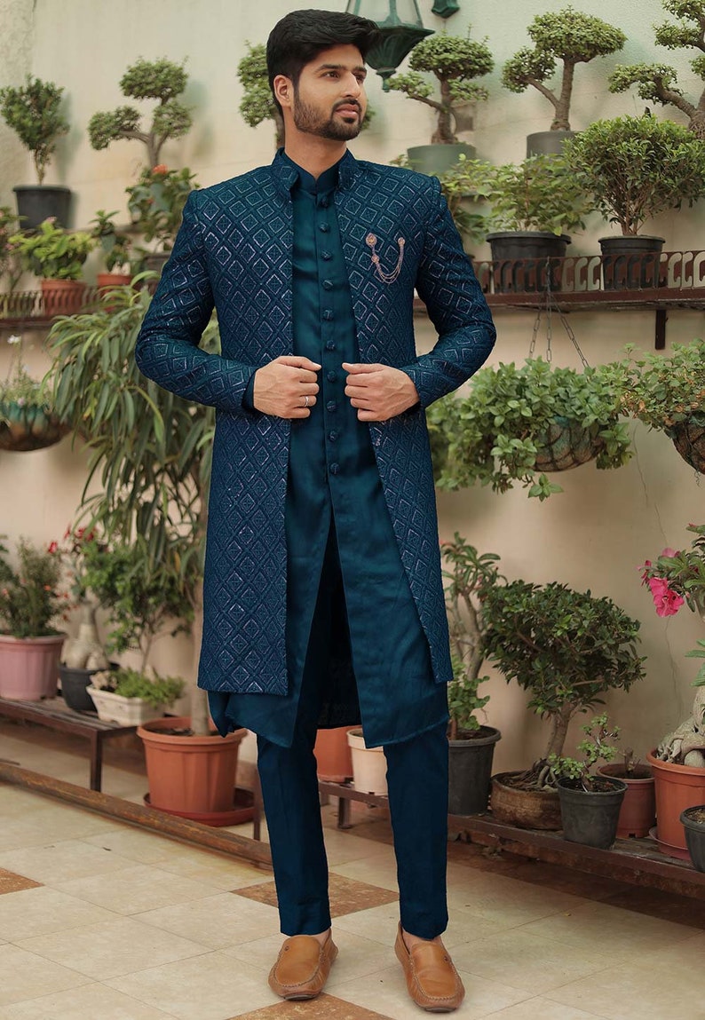 May include: A teal blue three-piece suit with a patterned jacket, a long teal blue shirt, and matching teal blue pants. The man is wearing brown loafers.
