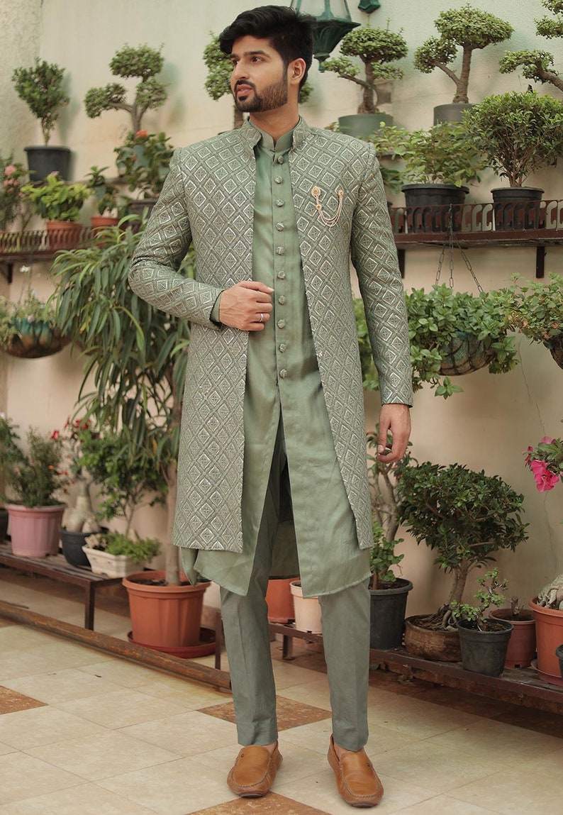 May include: A green patterned long jacket with a matching green shirt and pants. The jacket has a silver thread design and a gold button closure. The man is wearing brown loafers.
