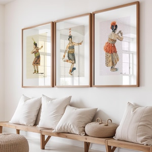 Op de afbeelding: Drie ingelijste prenten van dansers in traditionele kledij hangen boven een houten bank met kussens en een gevlochten mand. De prenten tonen figuren in kleurrijke kostuums, tegen een neutrale achtergrond, omlijst door lichtbruin hout.