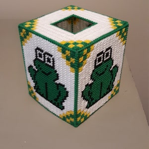 May include: A white tissue box cover with a green and yellow plaid pattern. The front and back of the box feature a green frog wearing glasses.