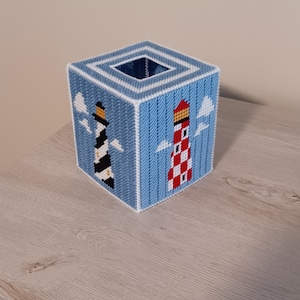 May include: A blue and white tissue box cover with a lighthouse design. The lighthouse is red and white with a black and white lighthouse on the opposite side.