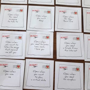 Peut inclure: Une collection de petits cartons carrés avec des messages manuscrits et des illustrations d'enveloppes. Chaque carte contient un message unique, comme "Ouvrez quand vous avez besoin de parler à quelqu'un" ou "Ouvrez quand vous avez besoin d'une pause d'Internet".