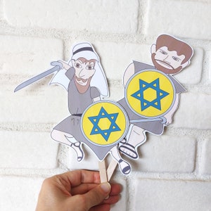 May include: Two paper puppets of people holding shields with a blue six-pointed star on a yellow background. The puppets are made of paper and have stick handles.