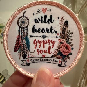 May include: A circular fabric patch with a light pink stitched border. The white centre features a dreamcatcher, a floral arrangement, and the text "wild heart, gypsy soul" with an arrow. A banner at the bottom displays "GypsyBlushTribe".