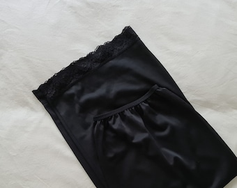 May include: Black slip with a lace trim at the top. The slip is made of a silky material and has a gathered skirt.