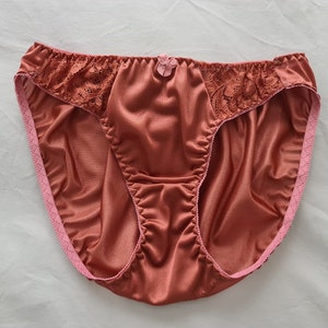 May include: A pair of rust-colored satin underwear with pink lace trim and a small pink flower detail.